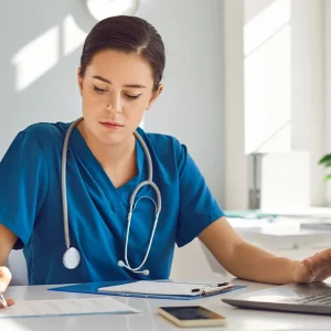 Young busy female nurse is concentrating on schoolwork while sitting at desk at workplace in clinic.