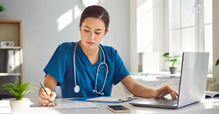 Young busy female nurse is concentrating on schoolwork while sitting at desk at workplace in clinic.