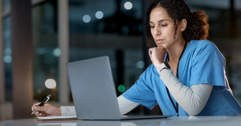 Nursing Instructor in Blue Scrubs Focuses Intently on Student Midterm Scores on Her Laptop