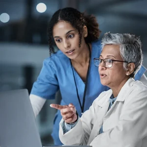 A nurse and a doctor use clinical judgment to discuss a patient plan on a laptop.