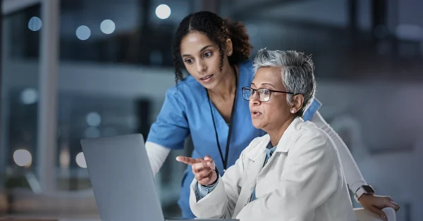 A nurse and a doctor use clinical judgment to discuss a patient plan on a laptop.